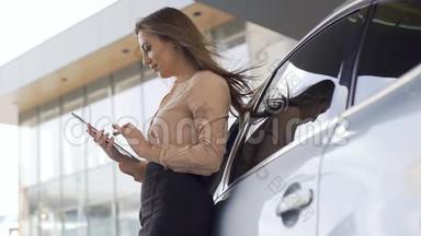 漂亮的<strong>销售经理</strong>站在汽车附近，在平板电脑上工作。 女商人